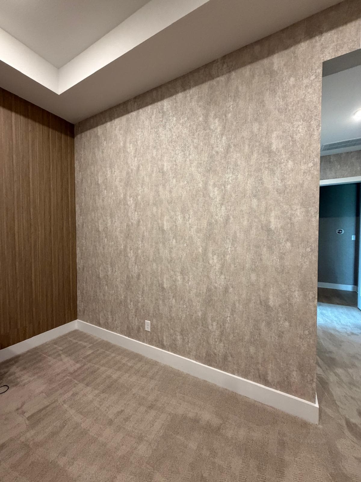 Textured beige wallpaper and vertical wood paneling meet in a room with patterned carpet.
